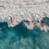 Trois surfeurs chevauchant des vagues turquoise vus du ciel