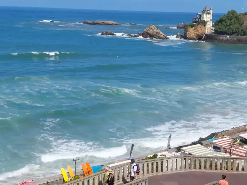 Côte rocheuse aux vagues bleues, terrasse de plage avec des chaises colorées et phare sur le littoral