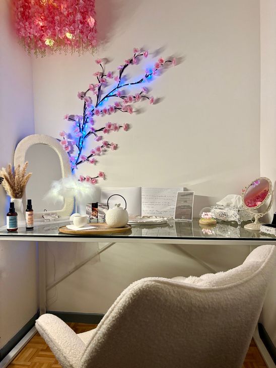 Un bureau blanc avec un miroir, une décoration murale en forme de fleurs de cerisier et un fauteuil blanc confortable.