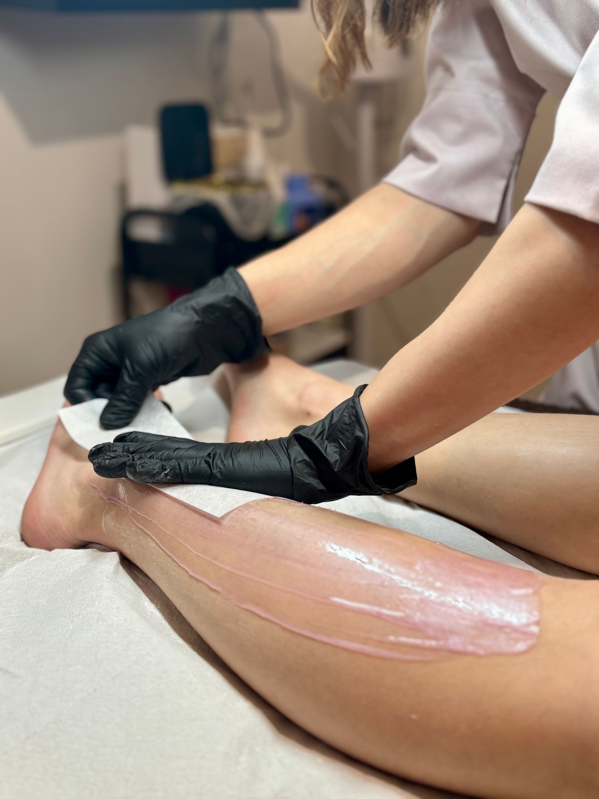 Dans une salle de soins, un professionnel applique une bande de cire sur le bas de la jambe d'une personne.