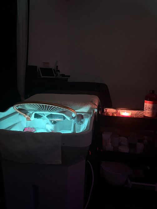 Une salle de spa à l'éclairage tamisé, avec un bac à pédicure bleu lumineux et une table de massage recouverte.
