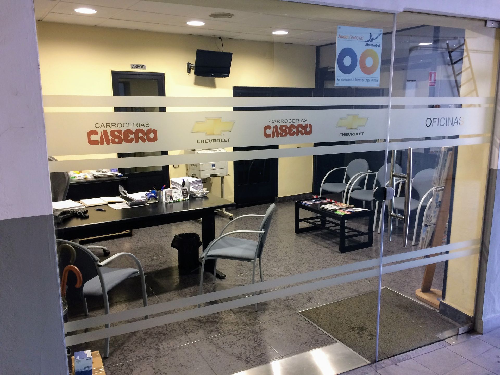 Oficina del área de servicio visible a través de una ventana; un coche en el garaje.