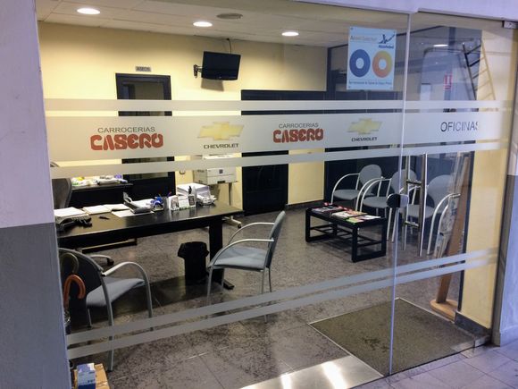 Oficina del área de servicio visible a través de una ventana; un coche en el garaje.