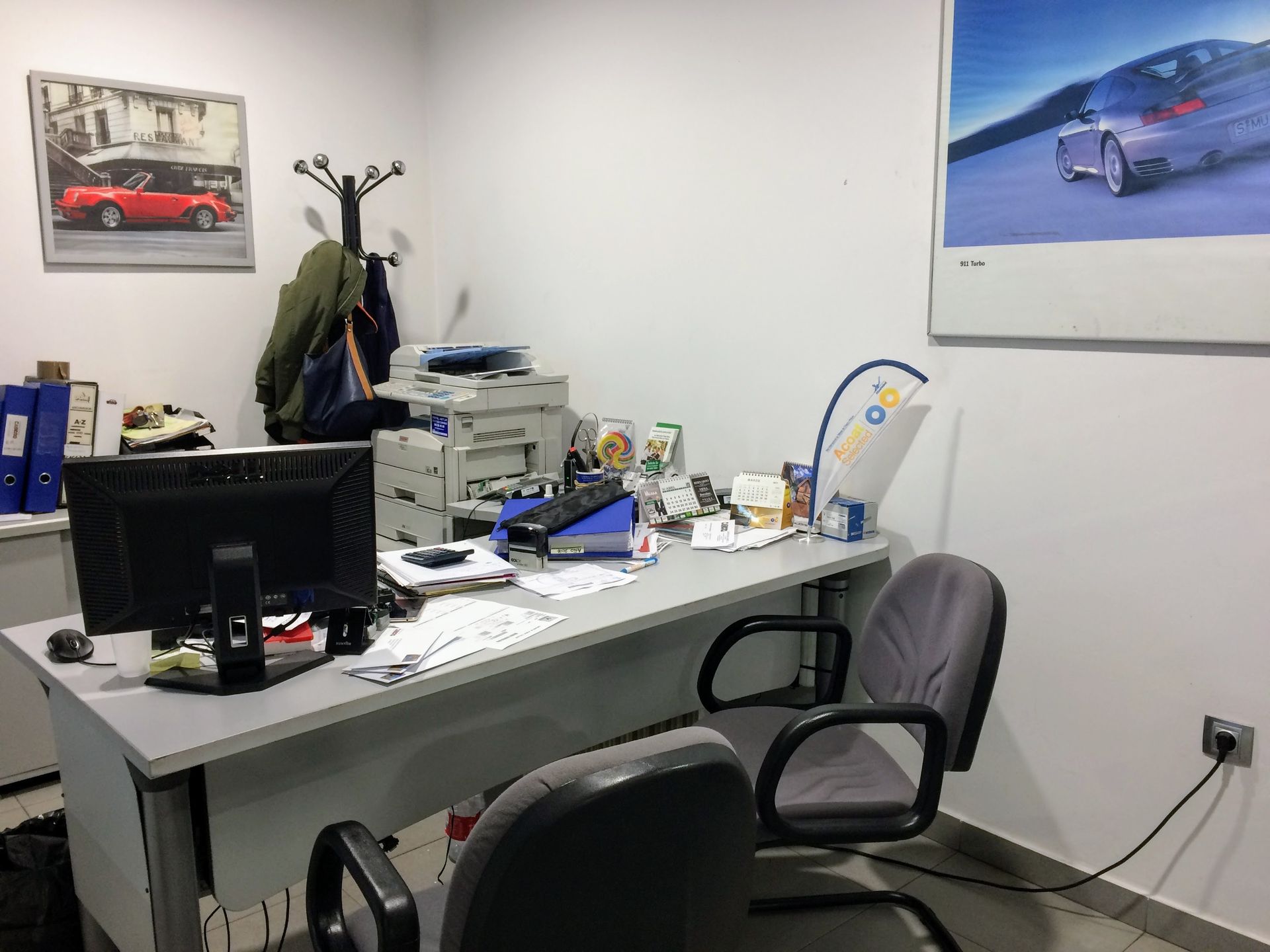 Coche plateado en un garaje con un coche rojo y otros vehículos. Entorno industrial con herramientas y equipo.