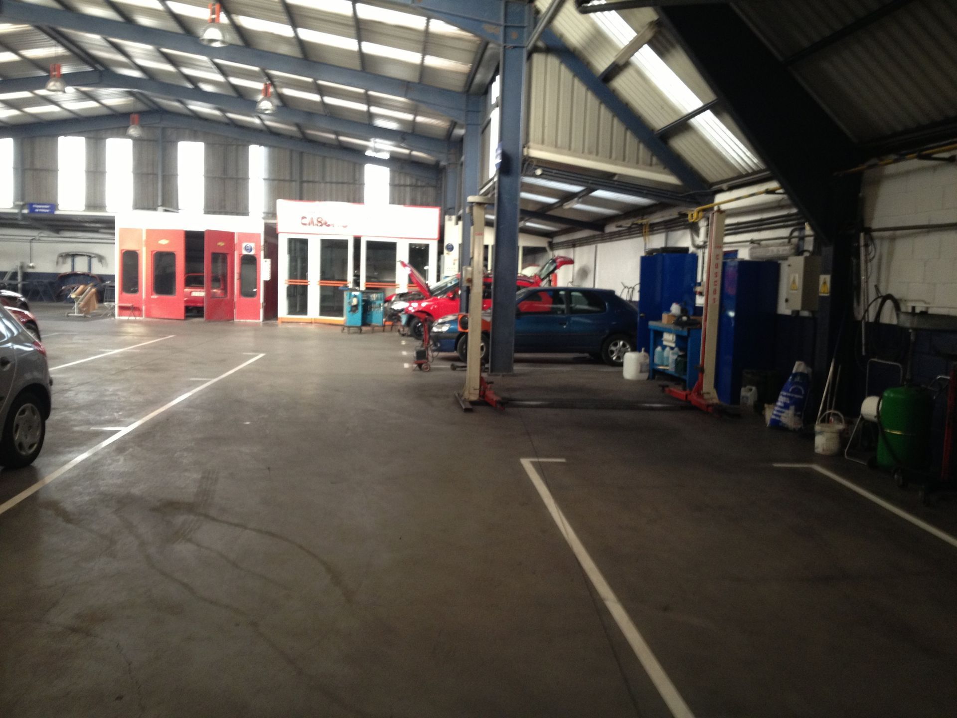 Dentro de un taller de reparación de automóviles con coches, elevadores y una cabina de pintura.