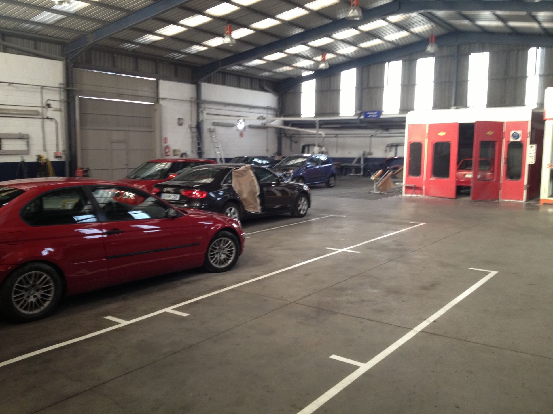 Autos en un taller de chapa y pintura; autos rojos, negros y azules estacionados. Se ve una cabina de pintura al fondo.