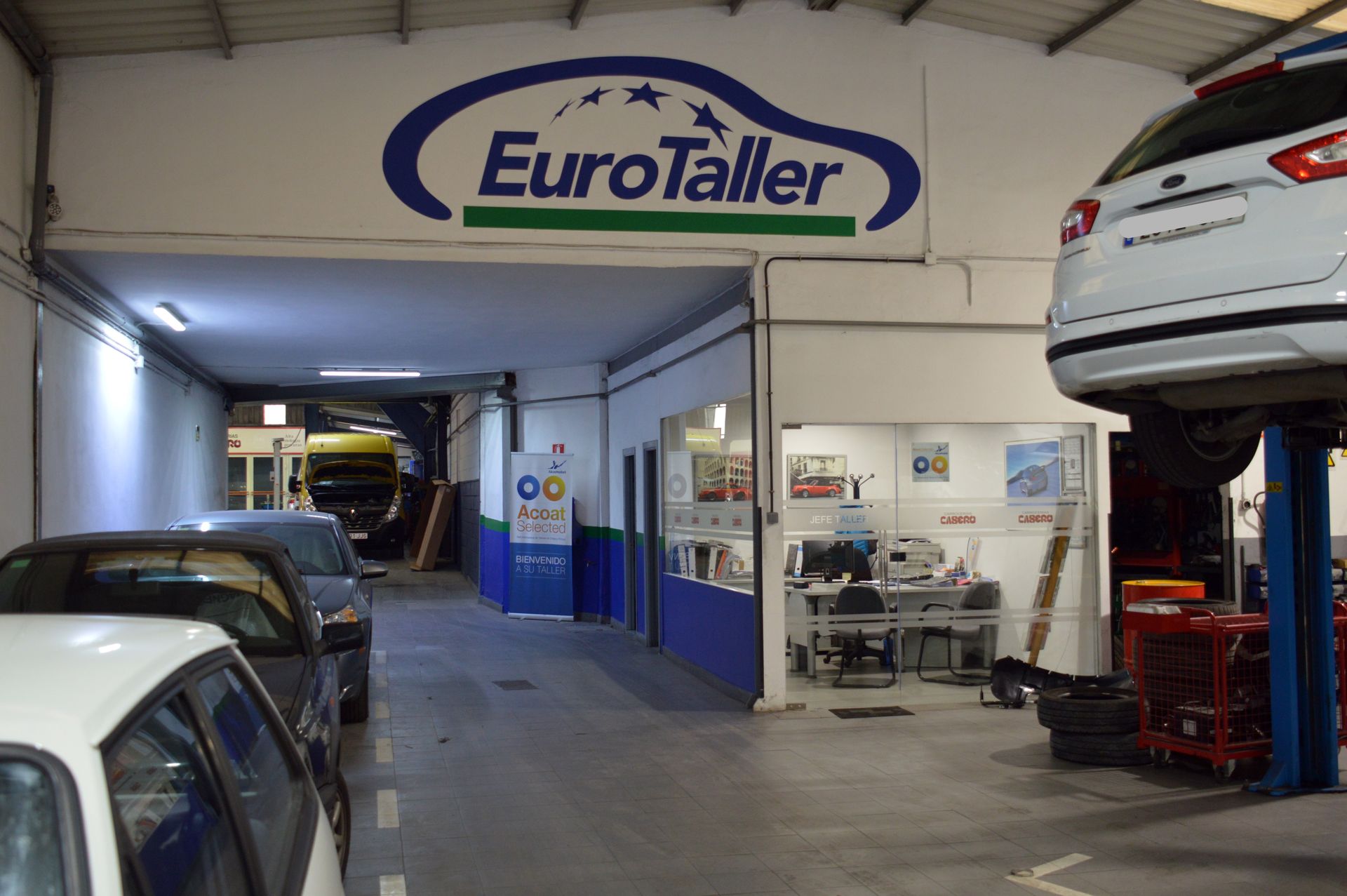 Coche rojo aparcado en un garaje con otros vehículos y equipos de reparación.