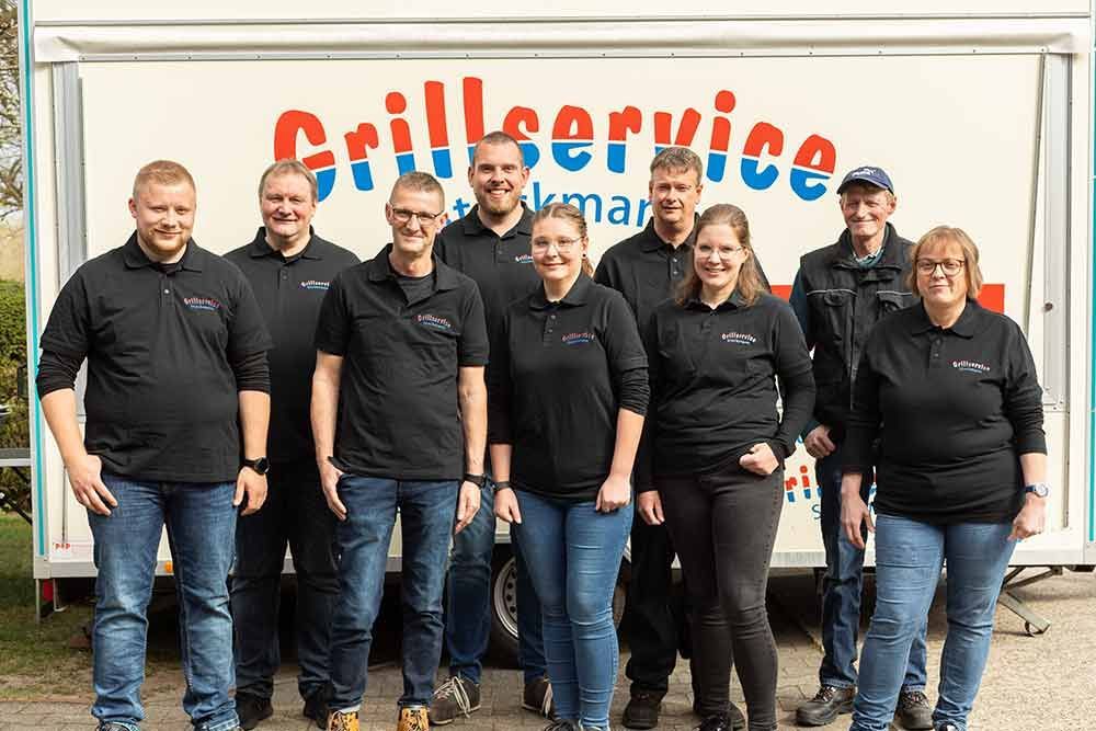 Eine Gruppe von Menschen posiert für ein Foto vor einem Grill-Service-Anhänger.