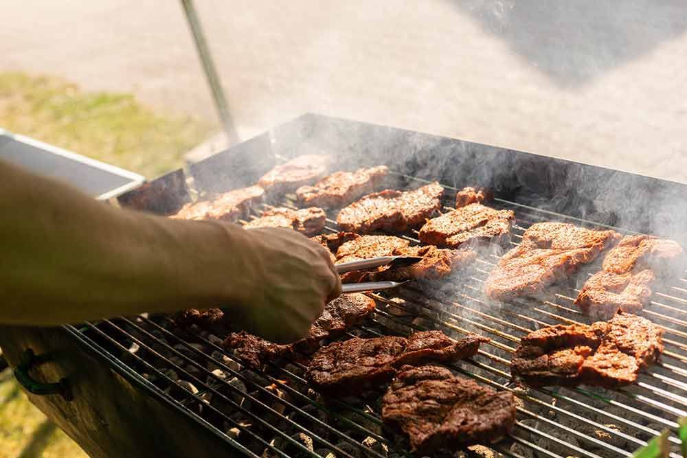 Eine Person grillt mit einer Zange Fleisch auf einem Grill.