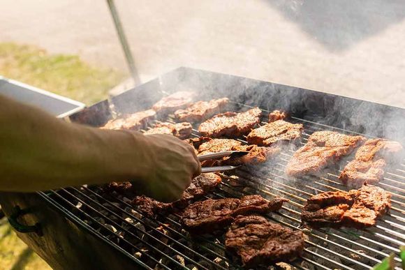 Eine Person grillt mit einer Zange Fleisch auf einem Grill.