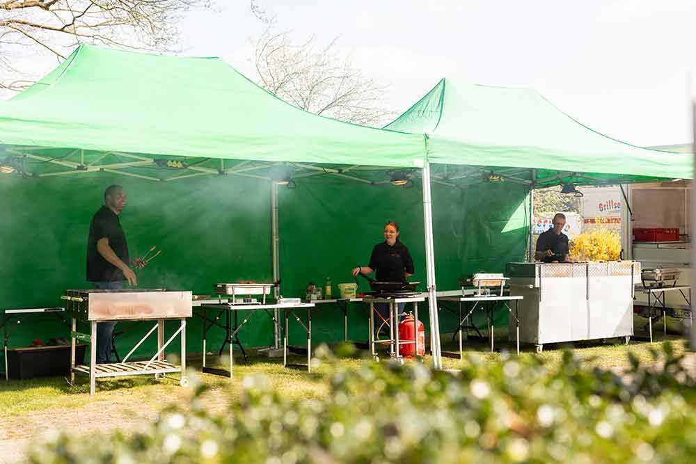 Eine Gruppe von Menschen kocht Essen unter einem grünen Zelt.