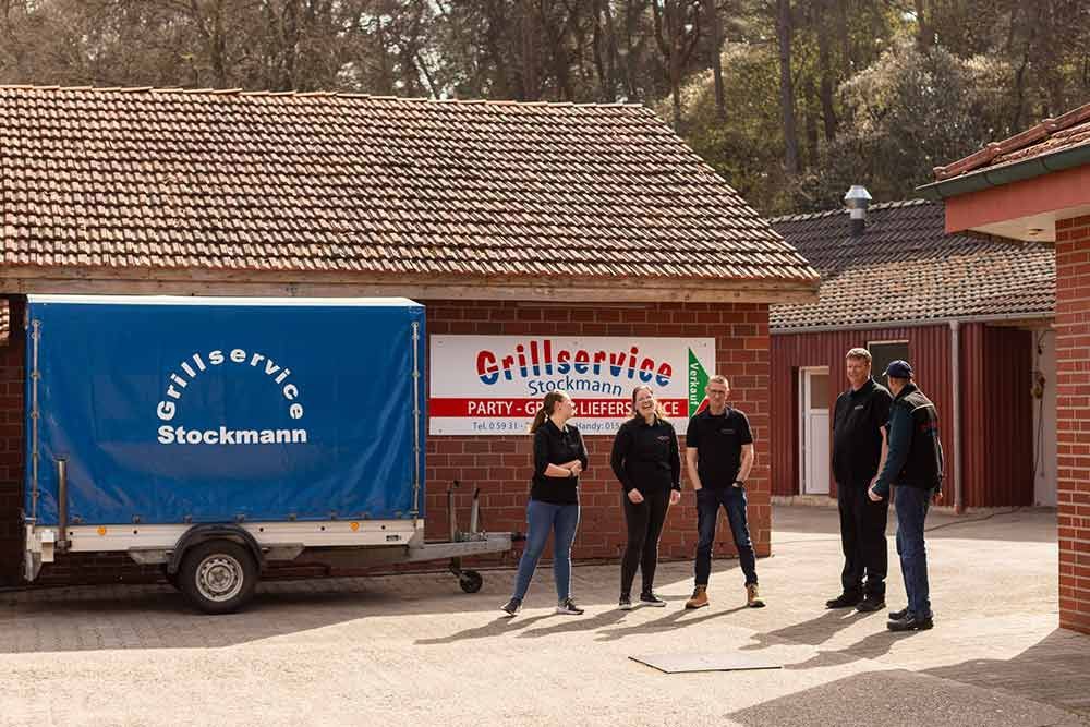 Eine Gruppe von Menschen steht vor einem Grillservice-Anhänger.