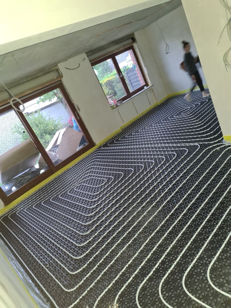 Schräge Ansicht eines leeren Raumes mit schwarz-weiß gestreiftem Teppich, Fenstern und einer Person an der rechten Wand