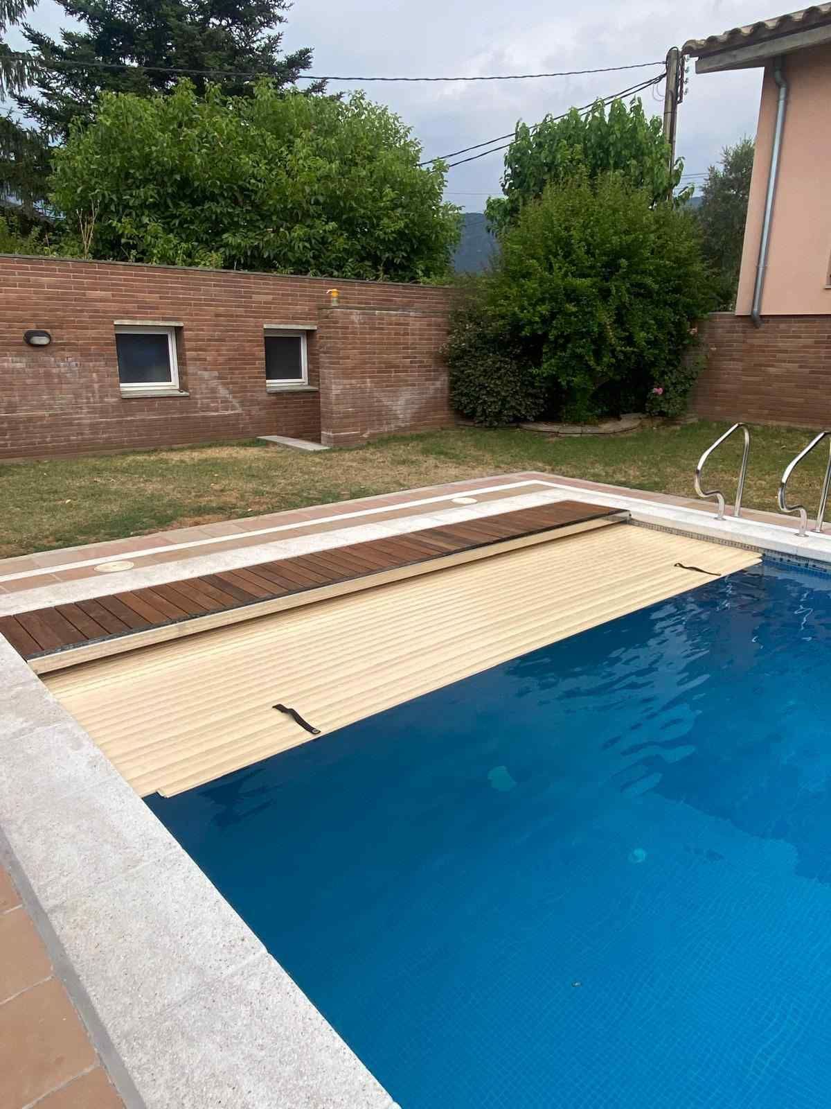 Una piscina en el patio trasero, parcialmente cubierta por una lona de seguridad de listones
