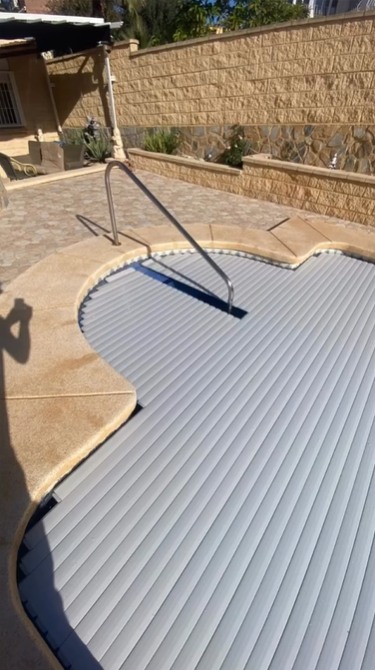Una cubierta automática de listones de color gris que cubre una piscina curva en el patio trasero