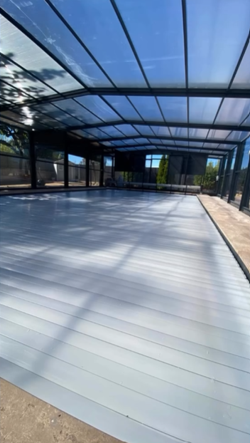 Una piscina exterior cubierta con un cerramiento translúcido, vista desde un ángulo bajo en un día soleado.