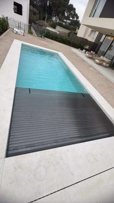 Una piscina rectangular con una cubierta de seguridad de listones de color gris oscuro parcialmente cerrada
