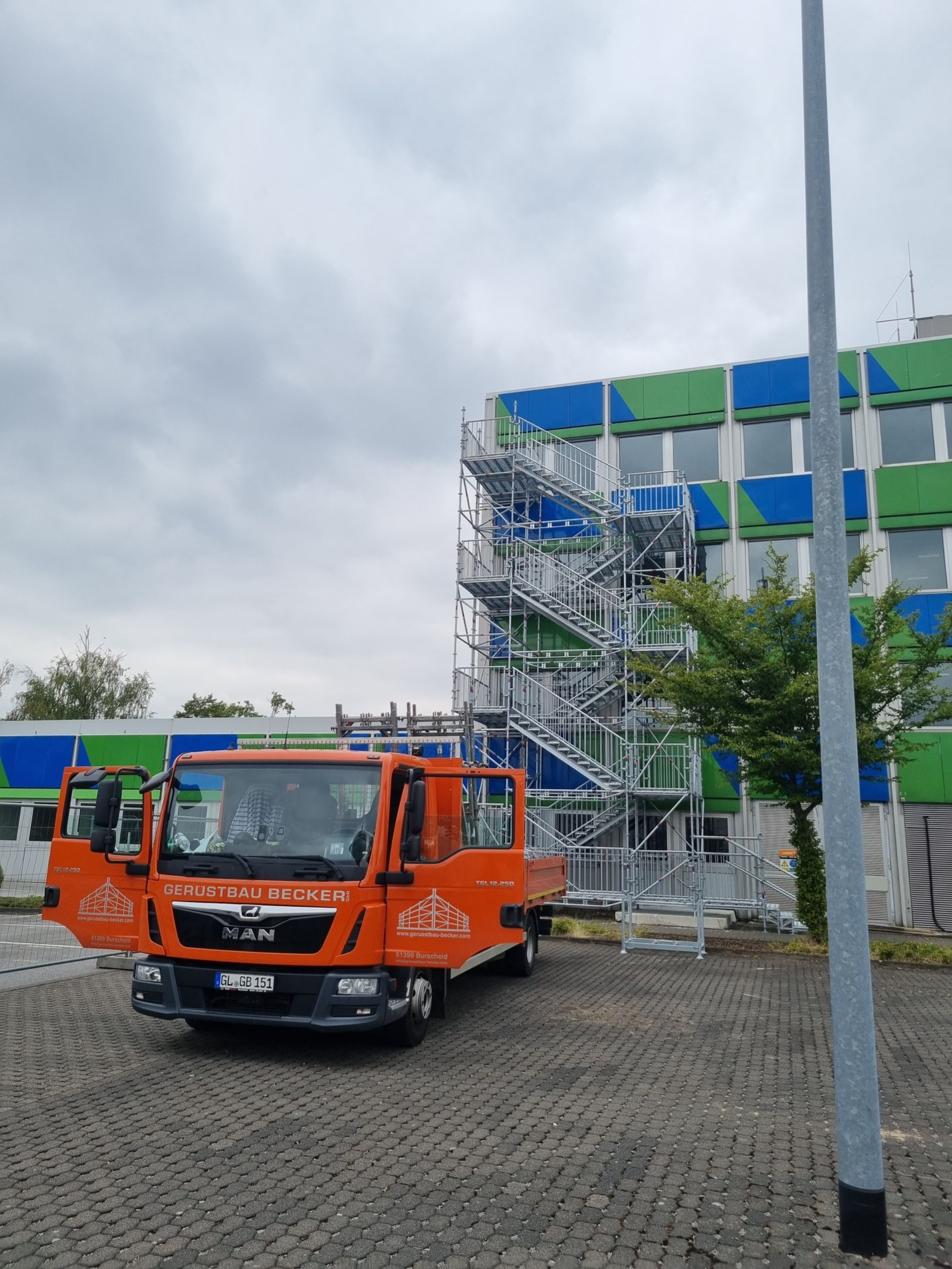 Gebäude mit Fassadengerüst und Bauunternehmen-Fahrzeugen.
