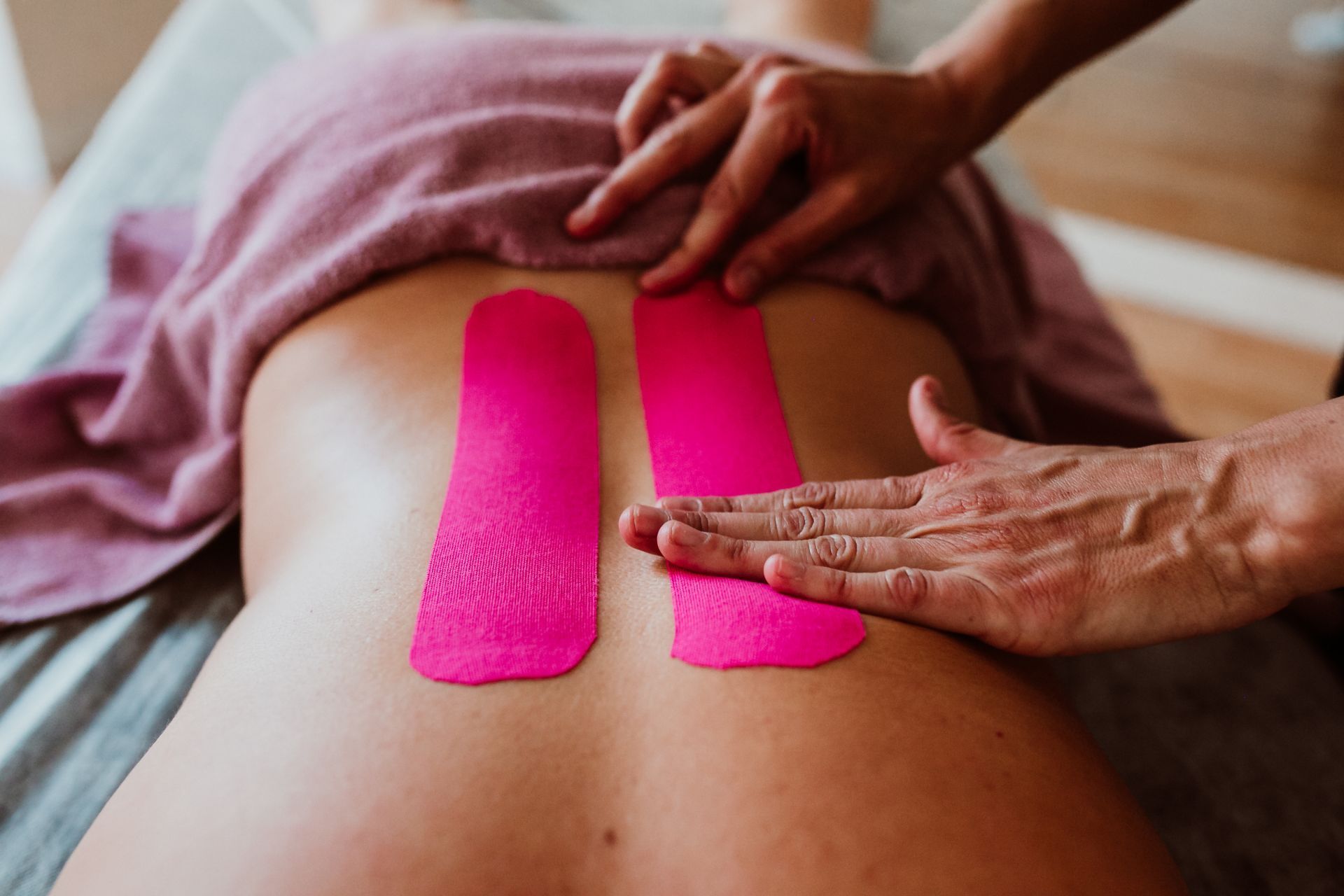 Espalda de una persona con tiras de cinta kinesiológica de color rosa aplicadas por la mano de otra persona.