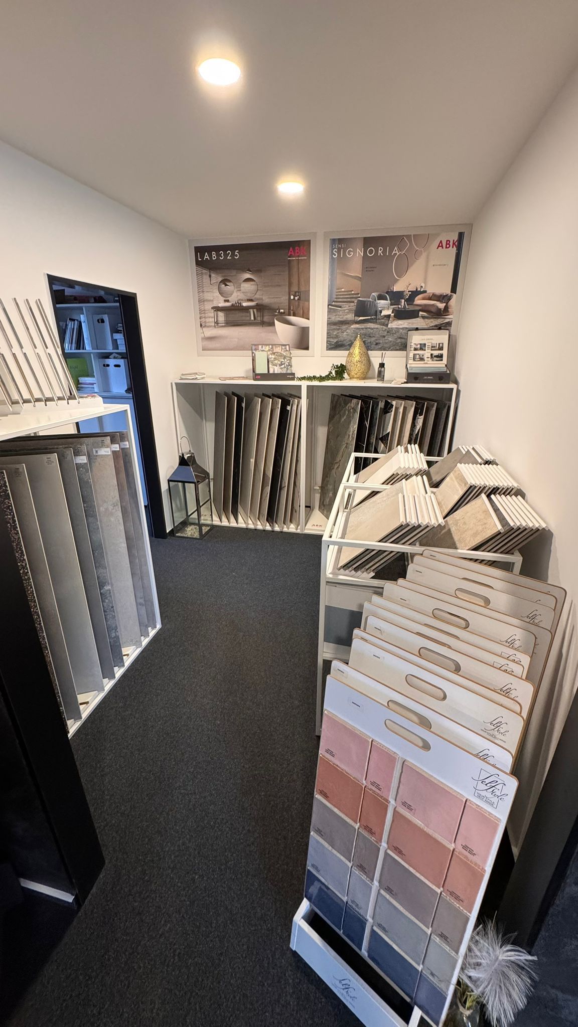 Ausstellungsraum mit Fliesenmustern in Regalen und Postern an der Rückwand.