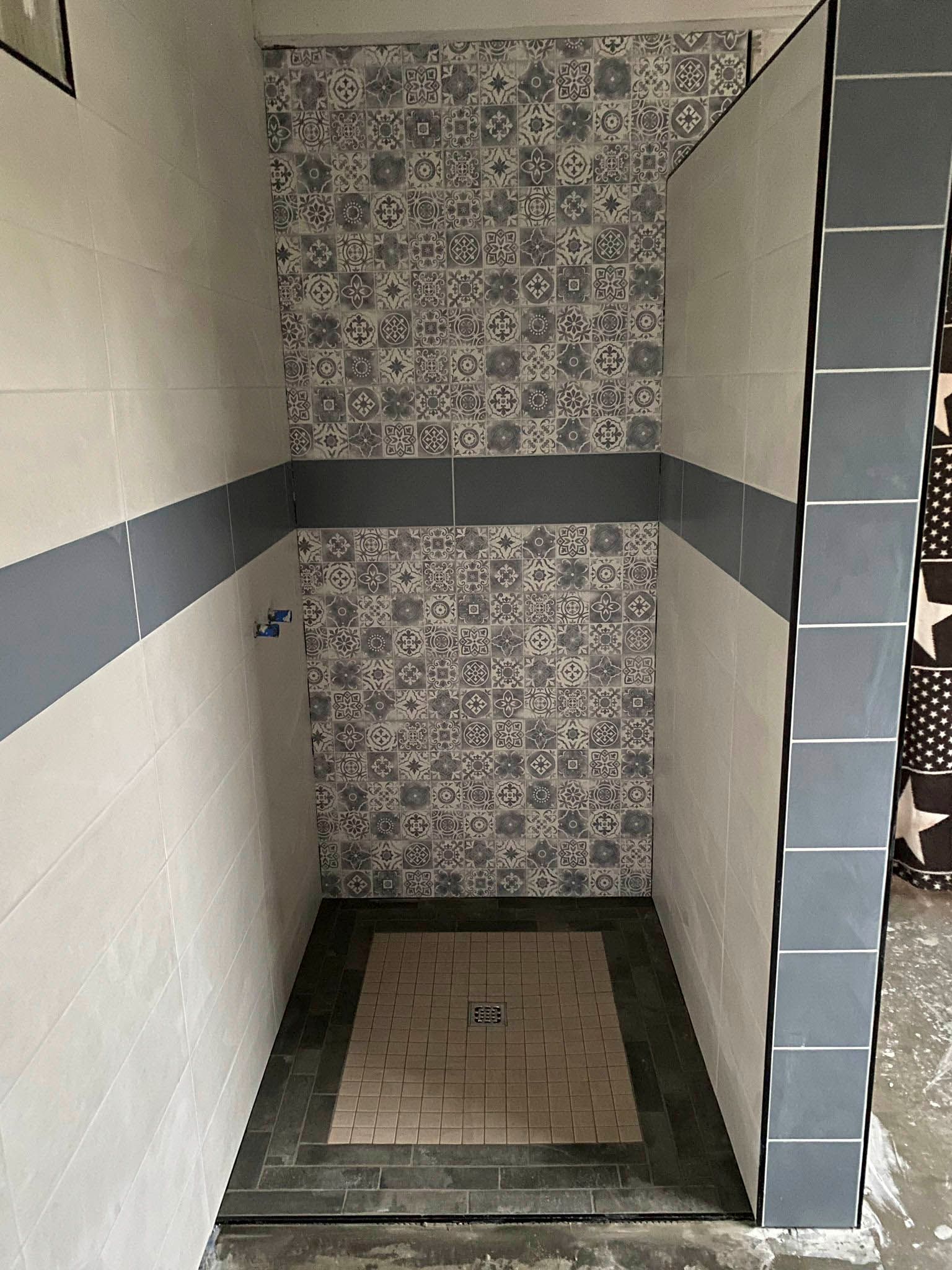 Geflieste Duschkabine mit gemusterter Akzentwand, dunkelgrünen Bodenleisten und hellgrauen Wänden.