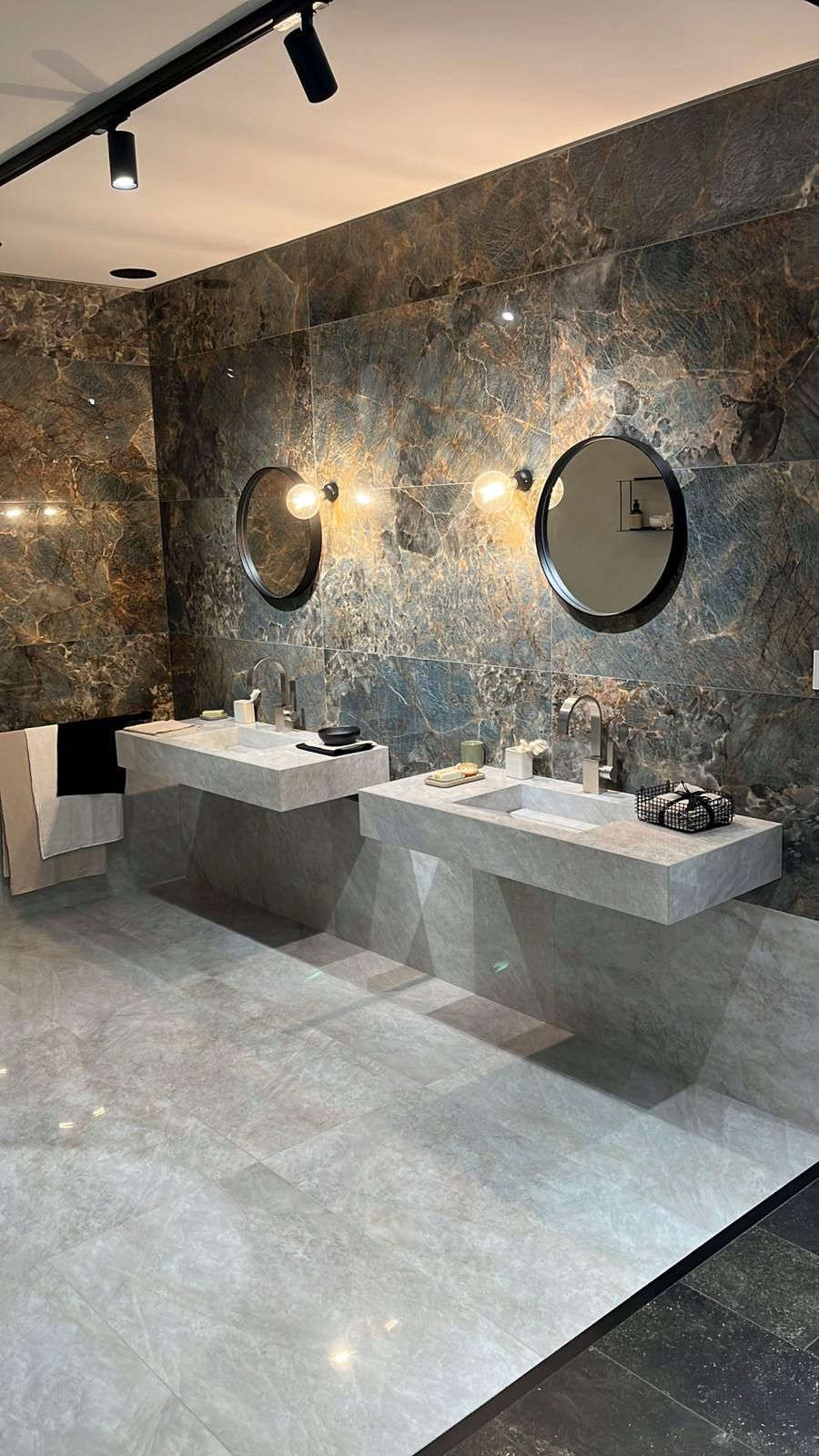 Badezimmer mit zwei freischwebenden Waschbecken, runden Spiegeln und dunkler, strukturierter Wand