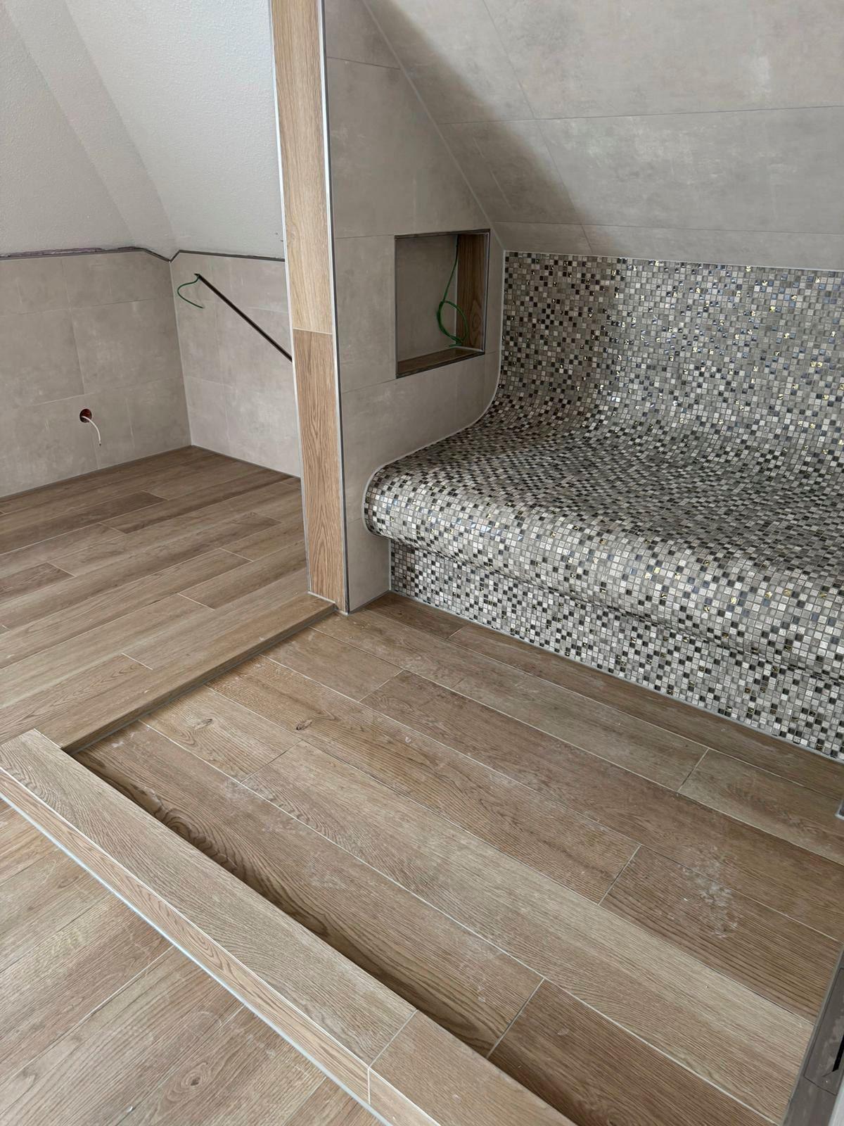 Zimmer mit Holzboden, Mosaikfliesenbank, Nische und schräger Decke; Bauarbeiten im Gange.
