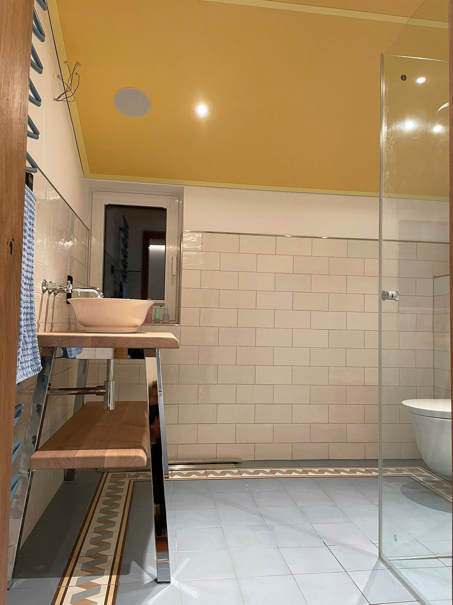 Badezimmer mit gelber Decke, weiß gefliesten Wänden, Glasdusche und schwebendem Waschtisch.