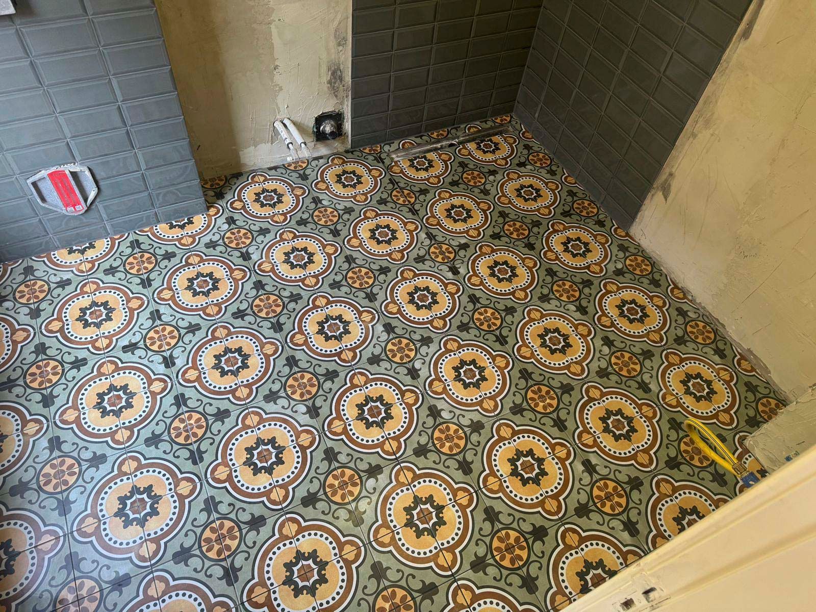 Badezimmer mit gemusterten Bodenfliesen, grauen Wänden und freiliegenden Rohrleitungen.