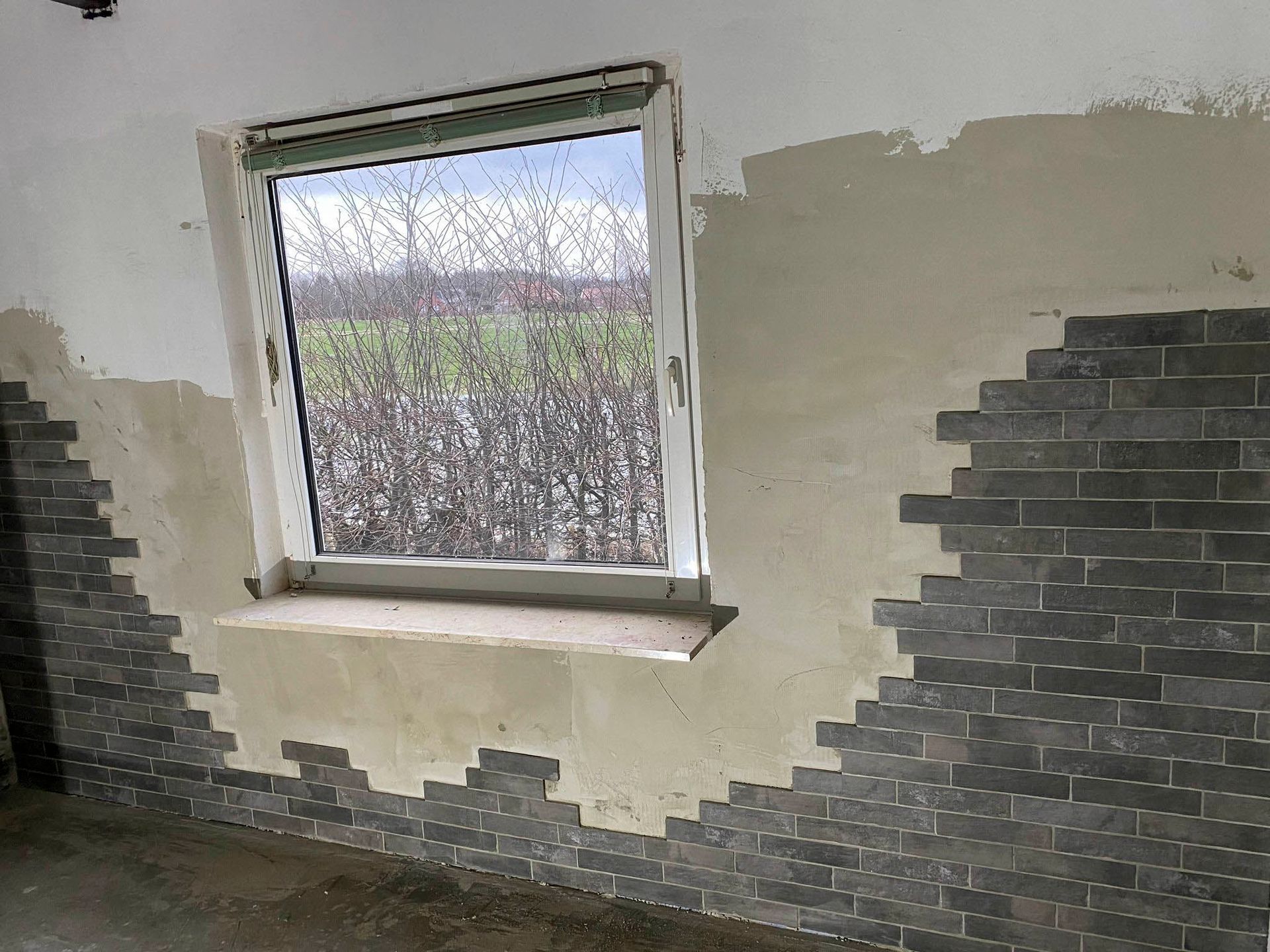 Innenraum mit Fenster. Graue Ziegelwände und teilweise verputzte Wand.