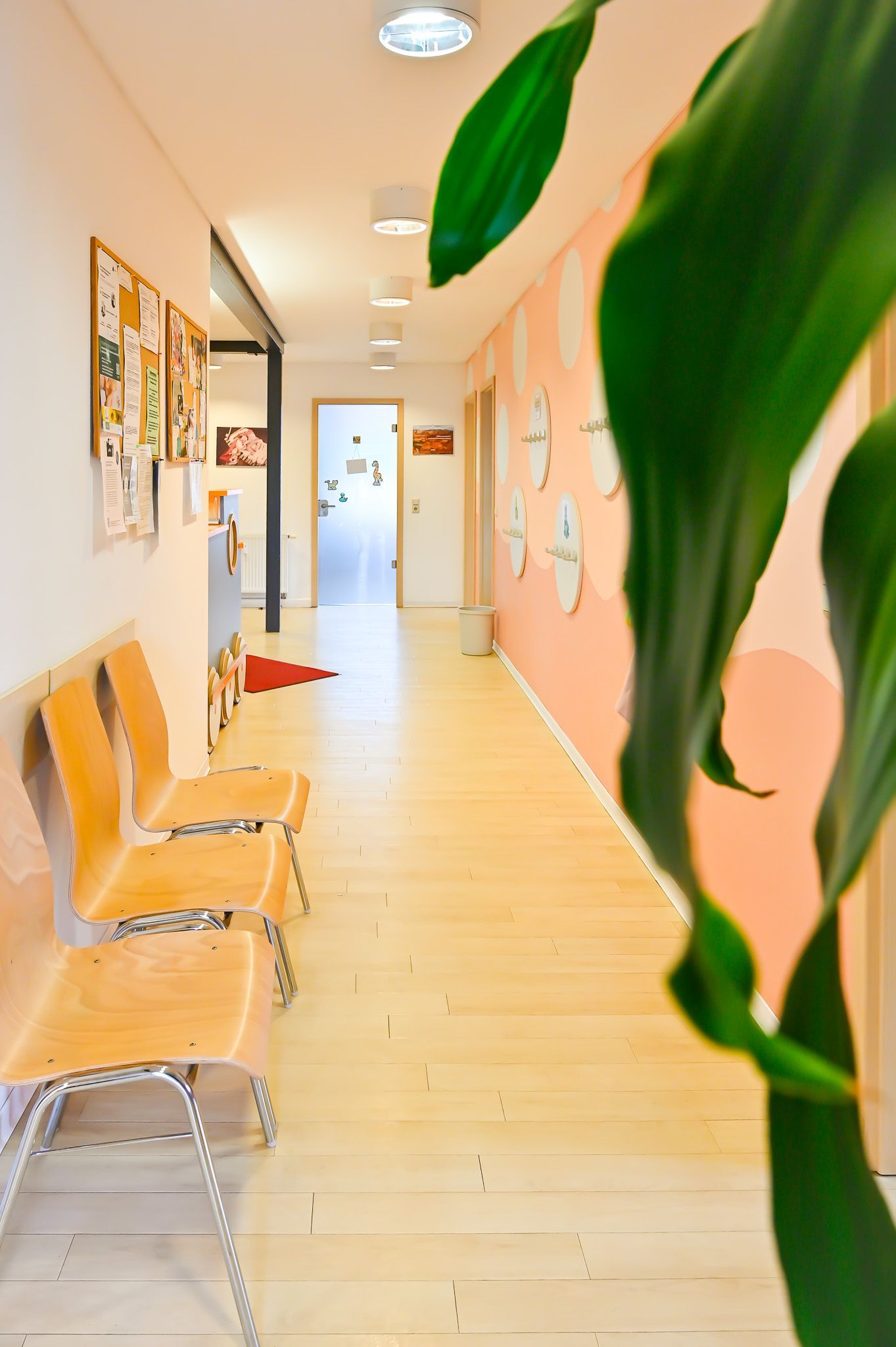 Langer Flur mit Holzboden, pfirsichfarbener Wand, Stühlen im Wartezimmer und einer Tür am Ende.