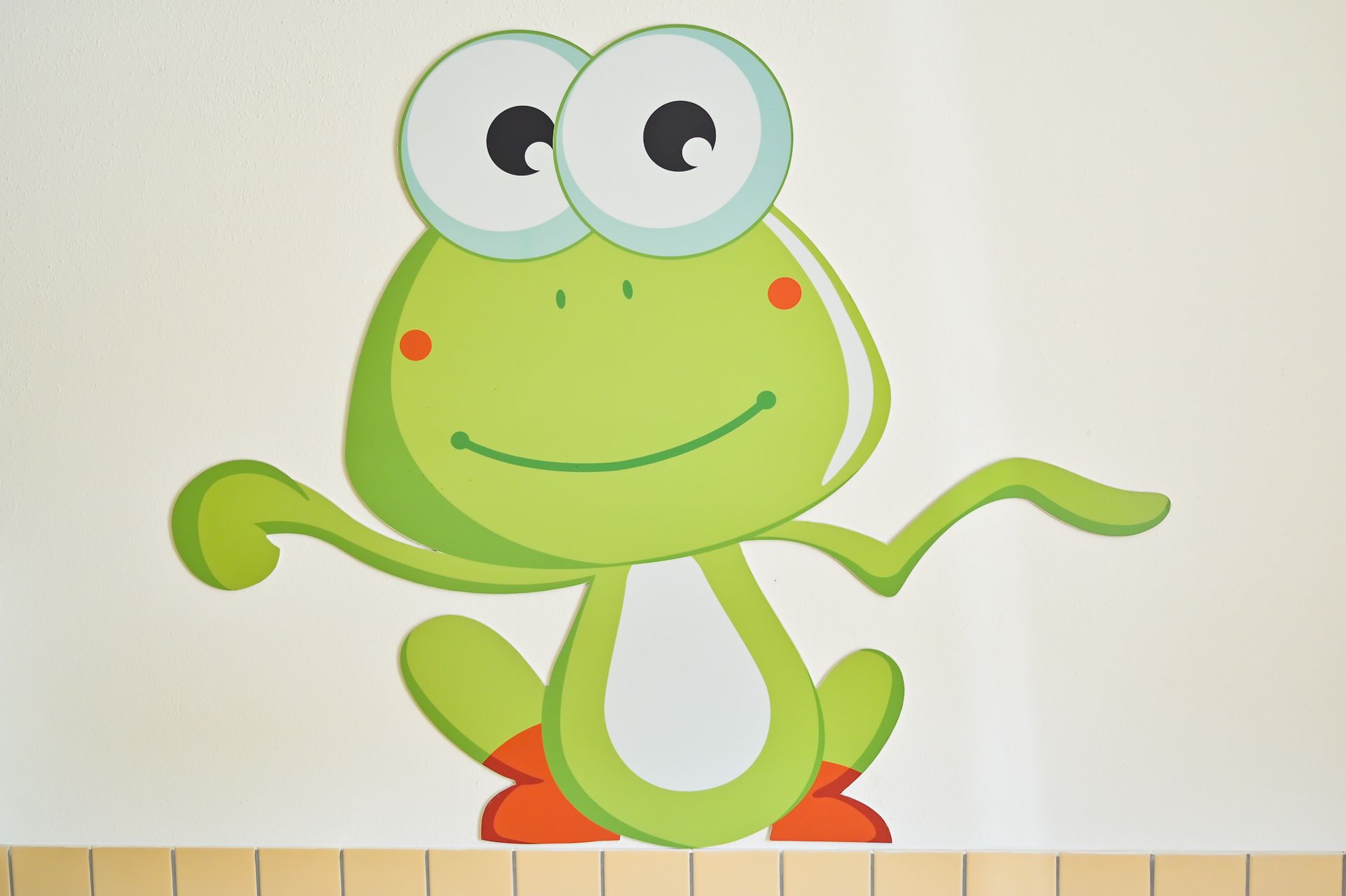 Grüner Cartoon-Frosch mit großen Augen und ausgestreckten Armen, lächelnd, rote Wangen, sitzend.