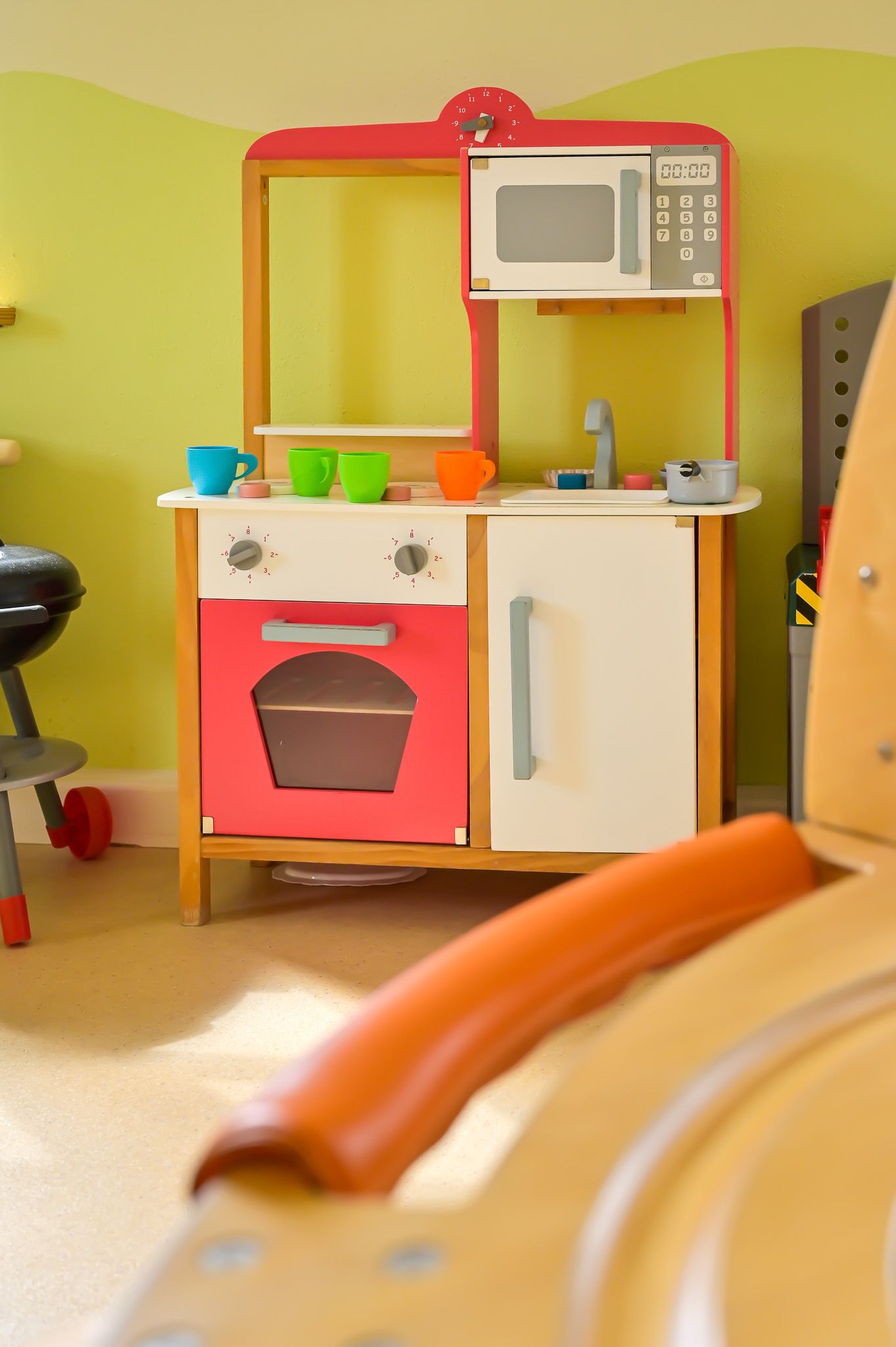 Spielküche mit Mikrowelle, Backofen und Spüle. Bunte Tassen auf der Arbeitsplatte.