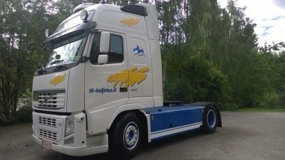 Valkoinen Volvo-puoliperävaunu sinisillä koristeilla pysäköitynä ulkona, logo kyljessä.