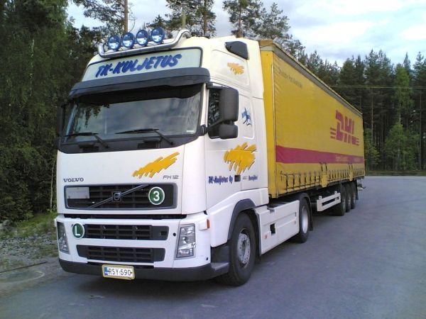 Valkoinen Volvo-kuorma-auto keltaisella perävaunulla pysäköitynä ulkona, AK-Kuljetus-logo näkyvissä.