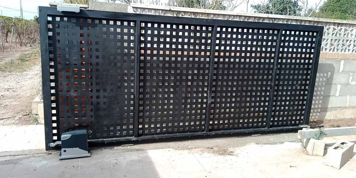 Una puerta negra con agujeros está al lado de una pared de ladrillos.