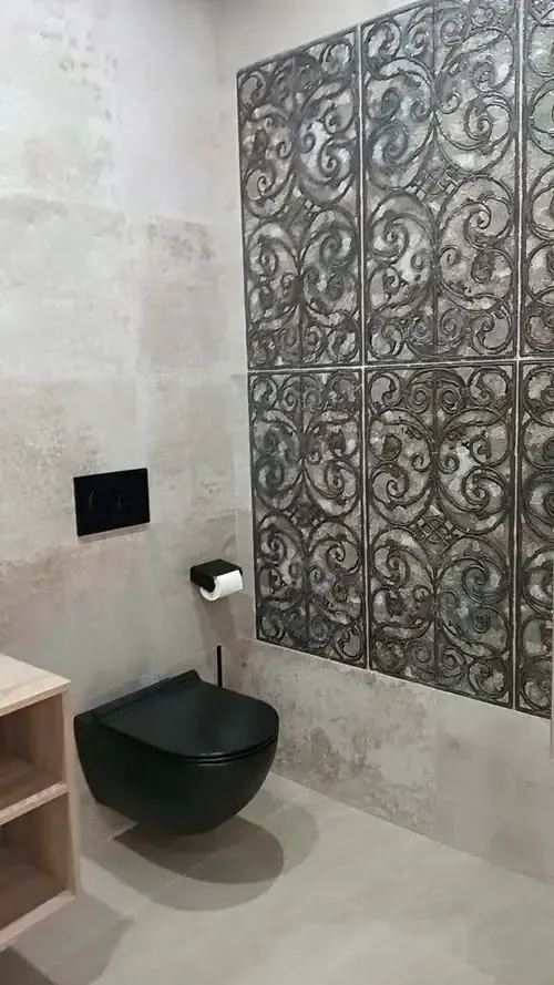 Baño moderno con inodoro negro, pared de azulejos decorativos, paredes neutrales.