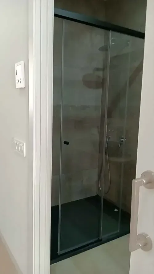 Interior de baño con mampara de ducha de cristal y paredes grises.