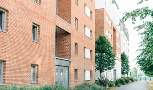 Edificio de apartamentos de ladrillo con hileras de ventanas y una pasarela al costado.