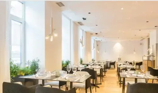 Interior de restaurante moderno y luminoso con mesas, sillas y grandes ventanales.