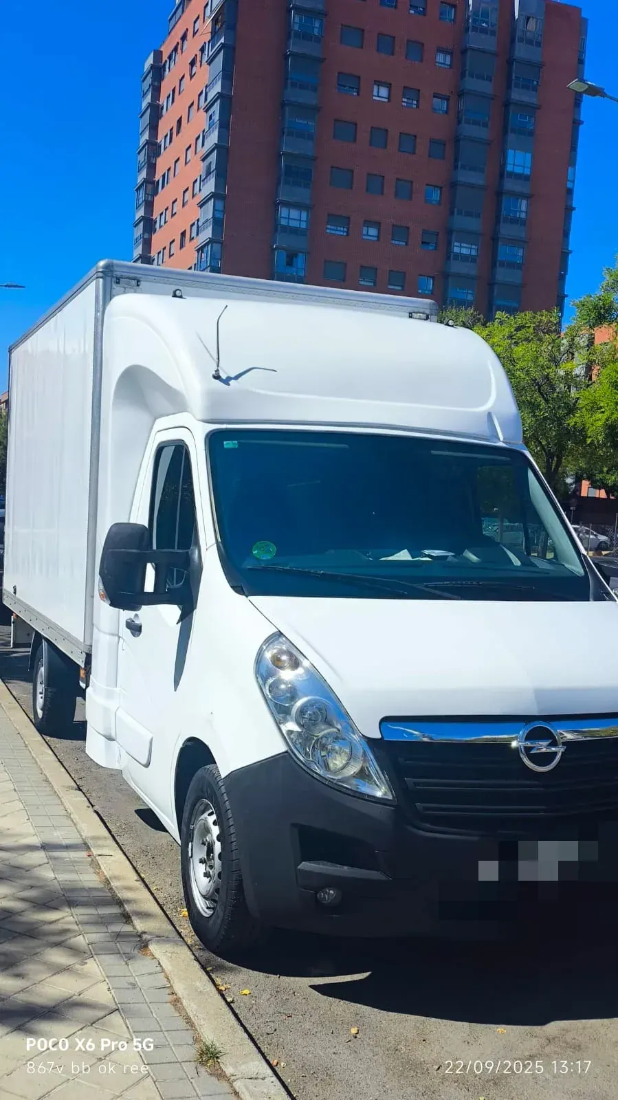 Camión Opel blanco estacionado en una calle frente a un edificio alto.