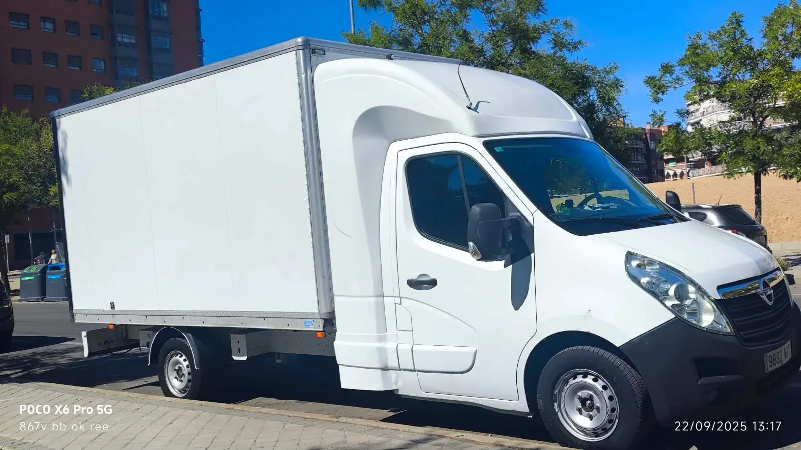 Furgoneta de carga blanca estacionada en una calle, probablemente para entregas, con un fondo de cielo azul.