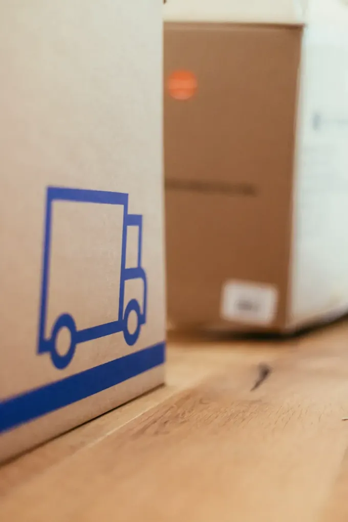 Cajas de cartón, una de ellas con un gráfico de camión azul, sobre un piso de madera.