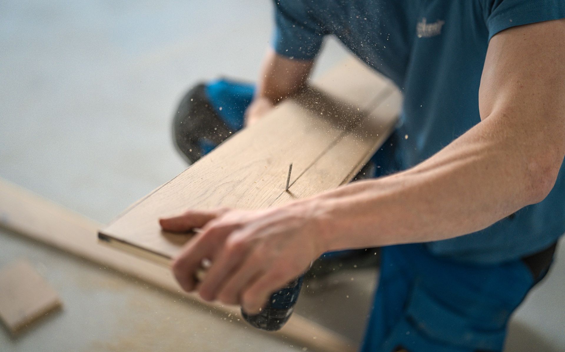 Gros plan d'une personne utilisant une perceuse pour visser un clou dans une planche de bois, avec des particules de sciure visibles dans l'air.