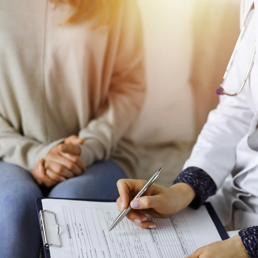 Un médico está escribiendo en un portapapeles mientras habla con un paciente.