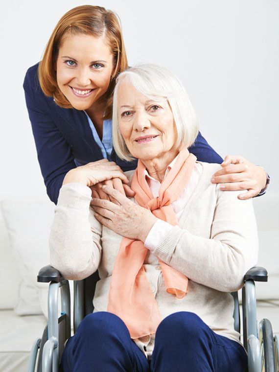 Eine professionelle Pflegekraft lächelt, während sie ihre Hände auf die Schultern eines älteren Menschen legt,