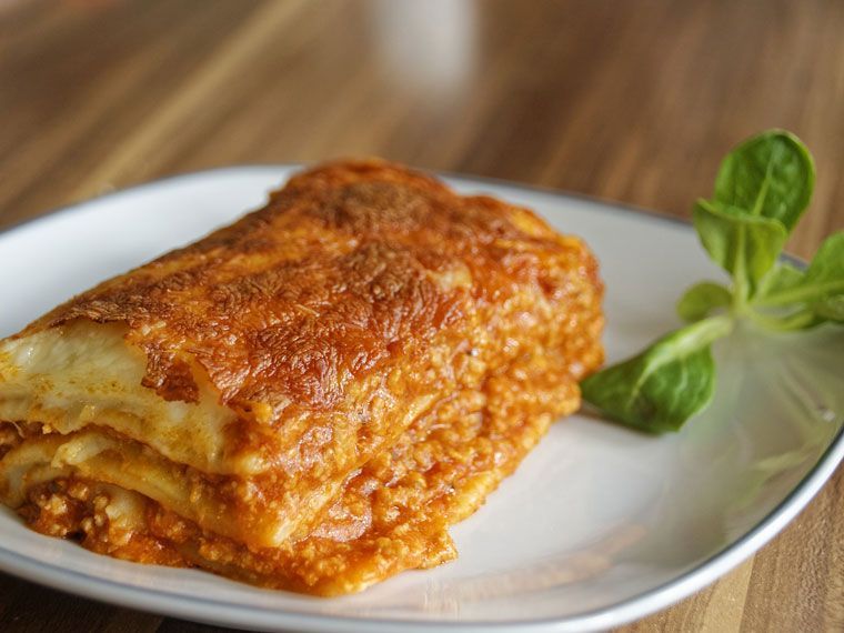Eine einzelne quadratische Portion geschichteter Fleischlasagne auf einem weißen Teller