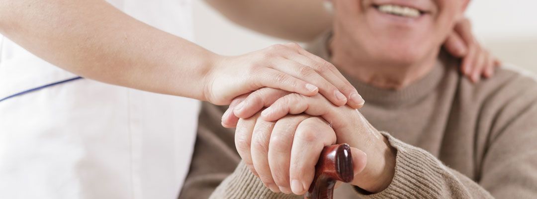 Eine Person legt sanft ihre Hand auf die Hand einer anderen Person, die den Griff eines Gehstocks hält.