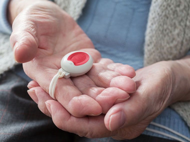 Eine lächelnde Frau steht hinter einer älteren Person, die in einem Rollstuhl sitzt, 