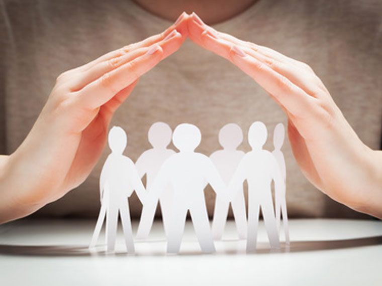 Hände, die wie ein Dach über einem Kreis aus weißen Papierfiguren gefaltet sind und Schutz, 